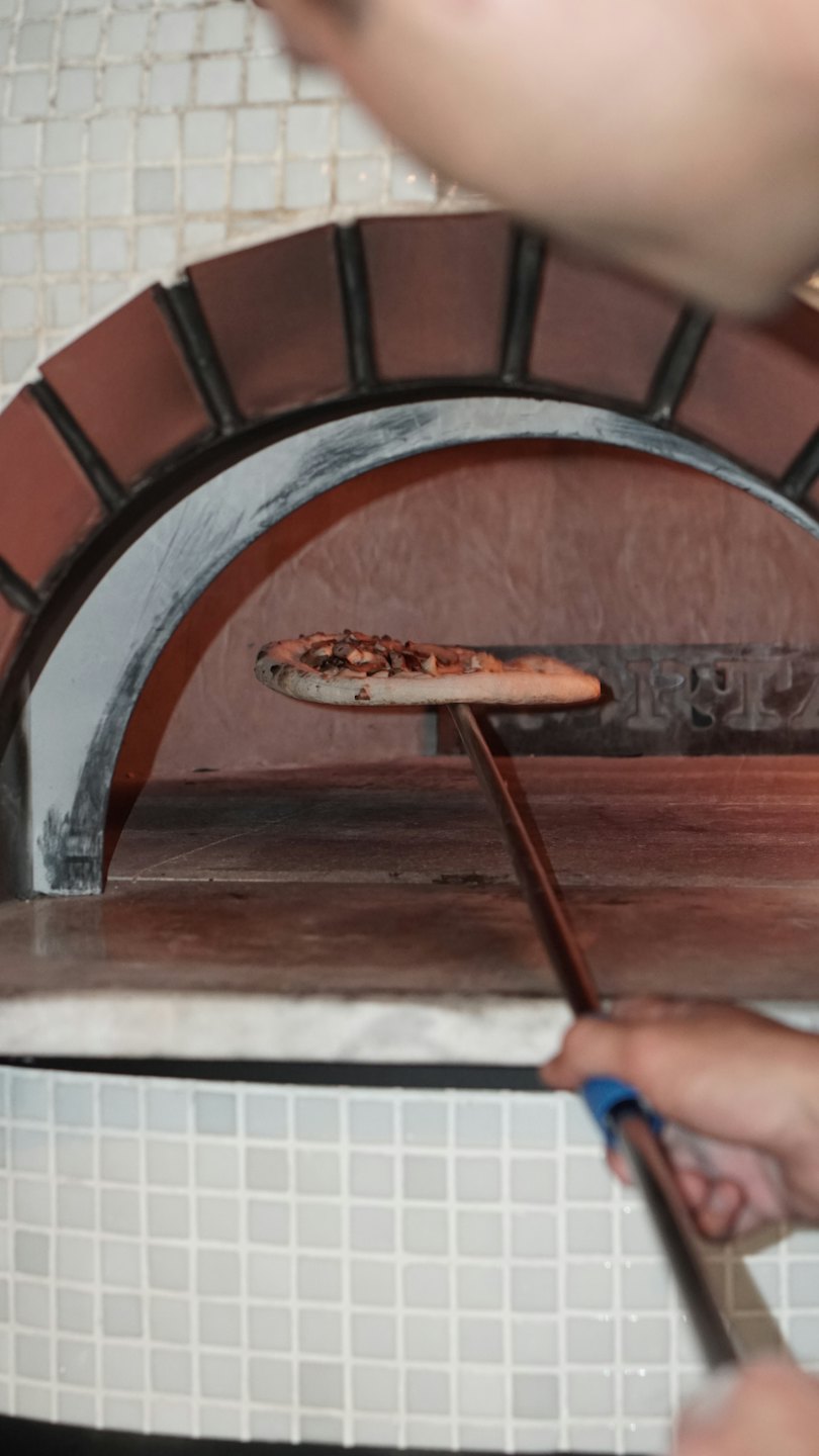 Hands sliding pizza into a hot brick oven.