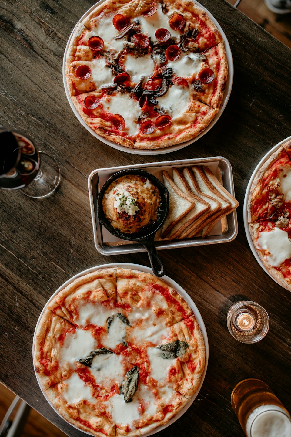 Three pizzas and an appetizer on a rustic table.