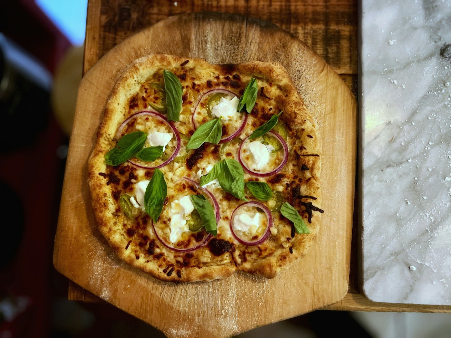 Artisanal pizza with basil and onion on a wooden peel.