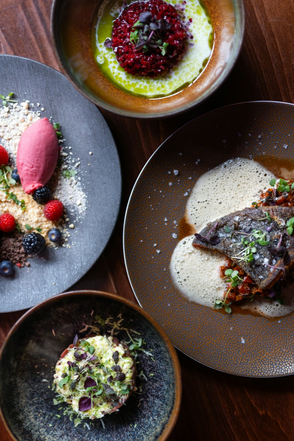 Four gourmet dishes are arranged on a dark wooden table.