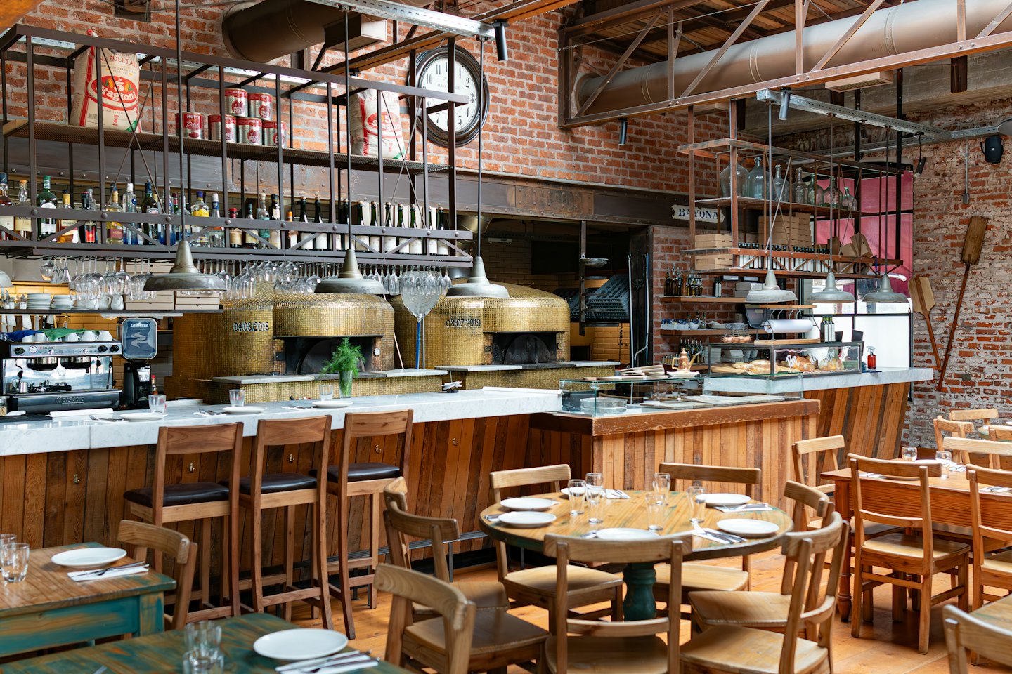 Two golden mosaic pizza ovens behind a marble counter in a restaurant.
