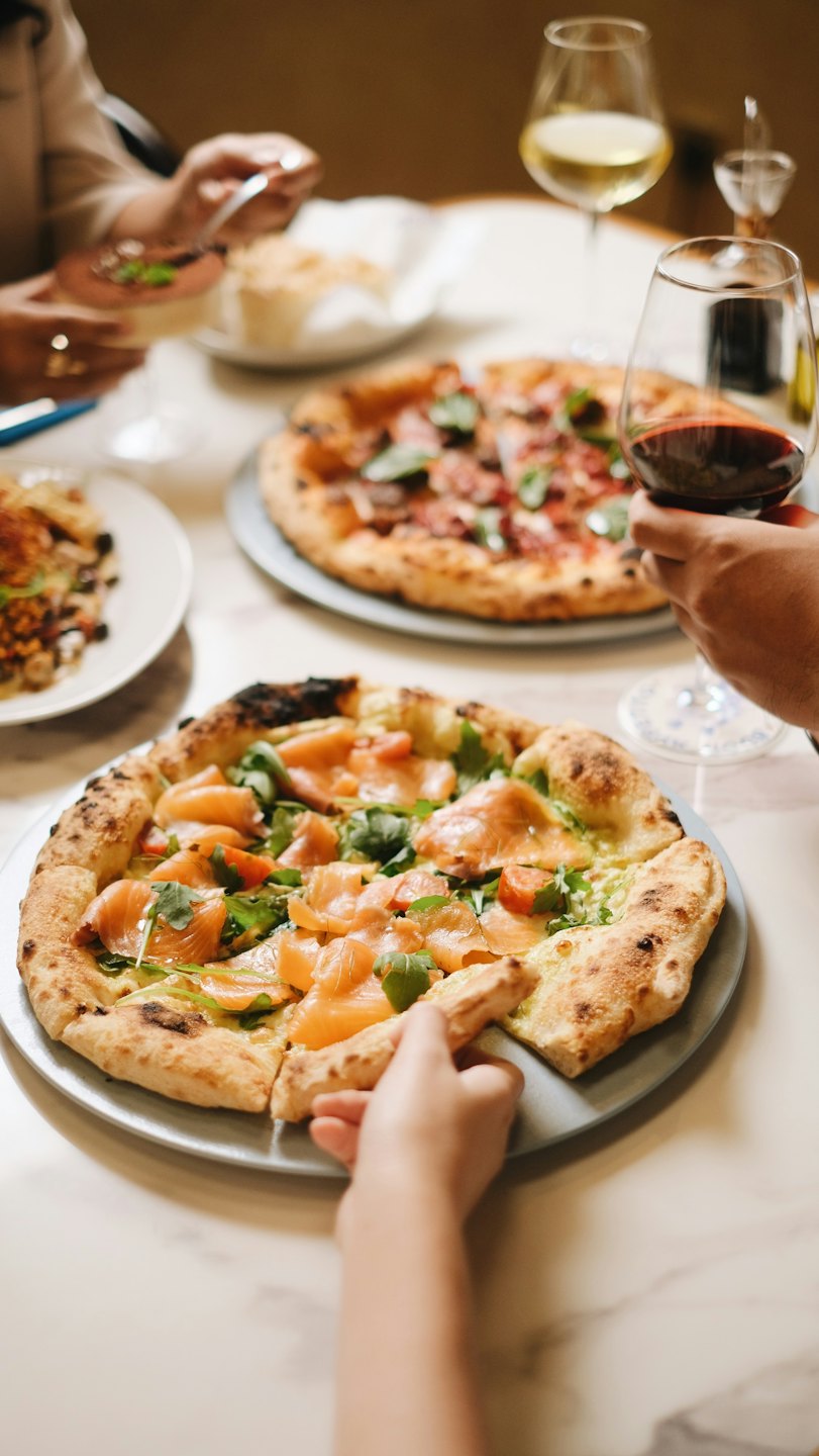 Friends sharing gourmet pizzas and wine at a dining table.